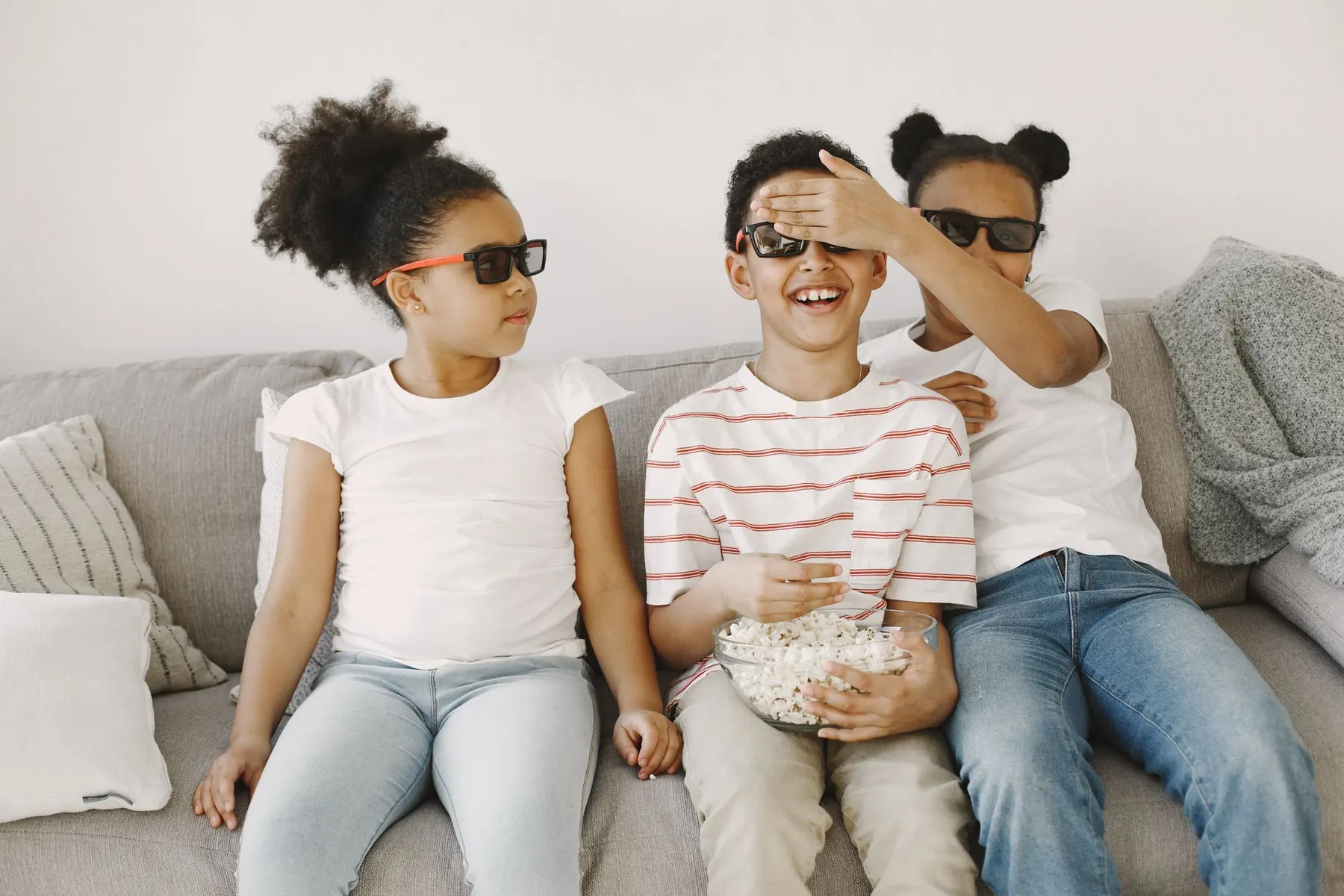 Three children on a couch eating popcorn